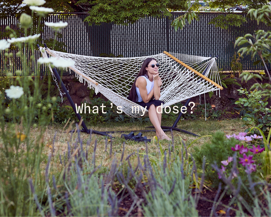 Person sitting on a white rope hammock in a garden surrounded by flowers and greenery, with the text “What’s my dose?” displayed across the center.