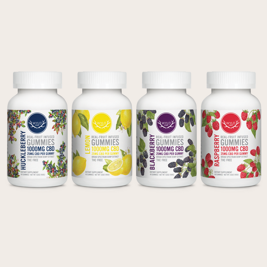 Four 40-count white bottles of Wyld CBD gummies arranged in a row on a light beige background. The bottles are labeled Huckleberry, Lemon, Blackberry, and Raspberry, each with a white cap and a colorful label showing the fruit illustrations.