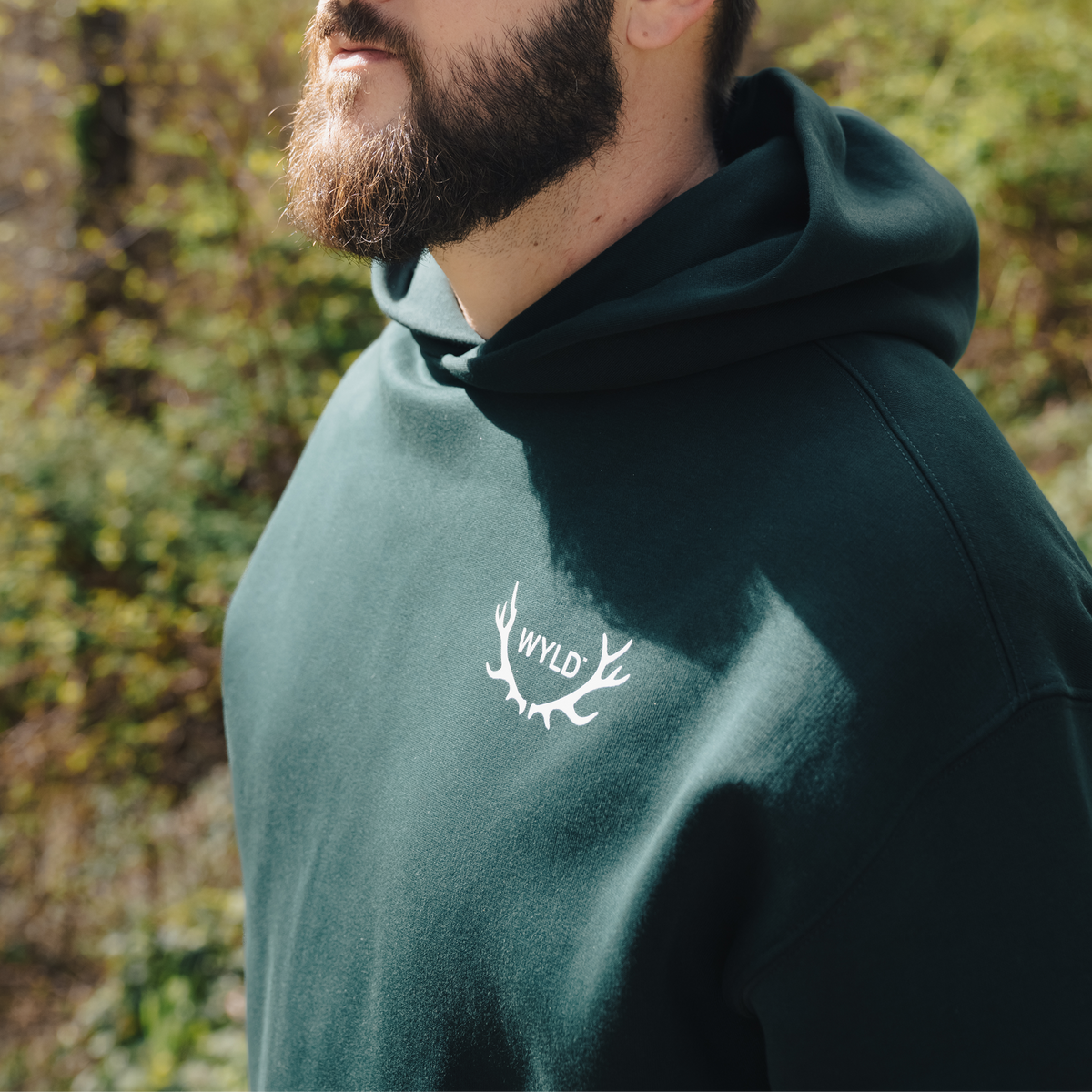Man wearing a green hoodie with 'WYLD' logo outdoors